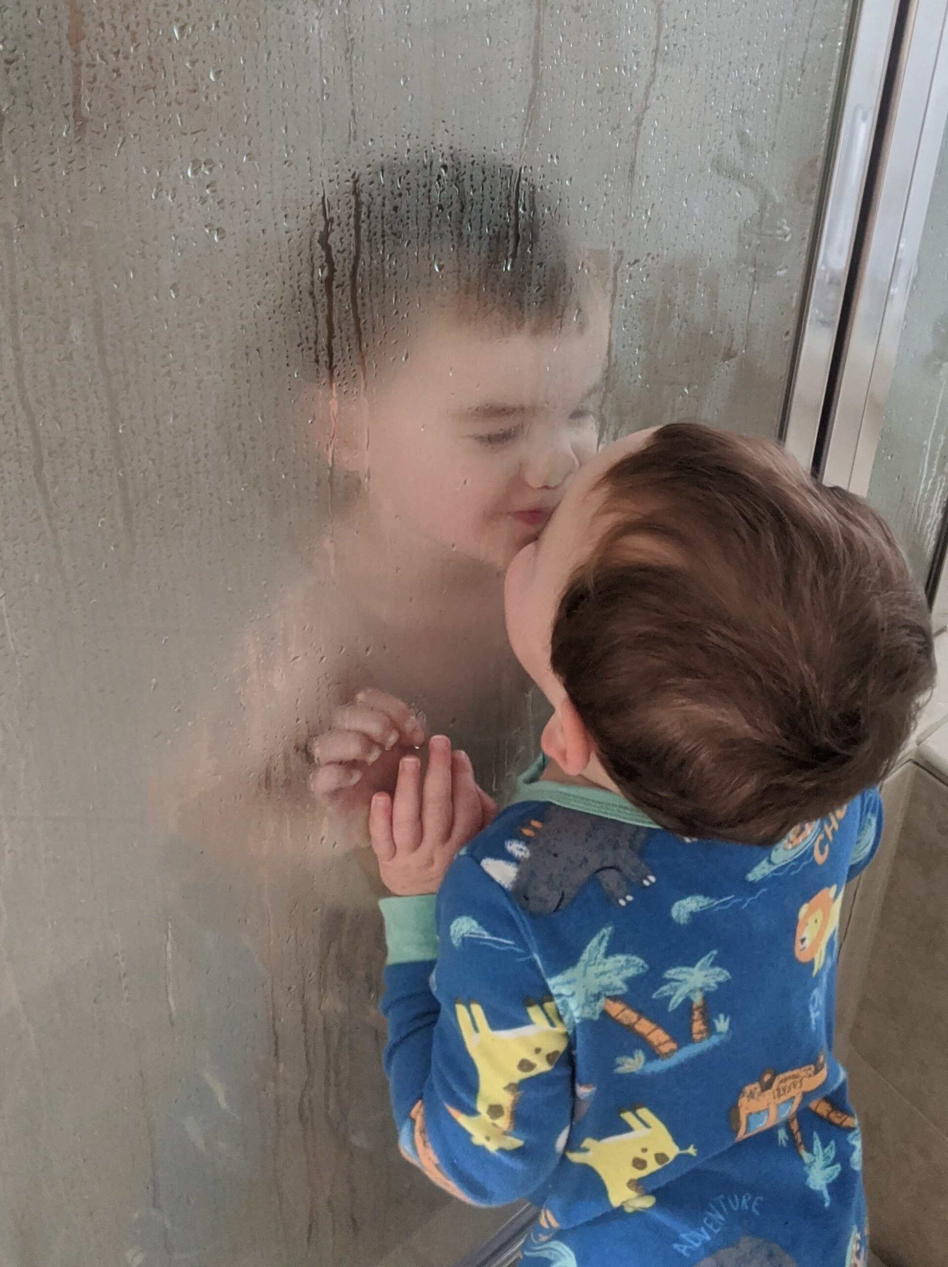 Twin brothers kissing each other on different sides of the shower door 