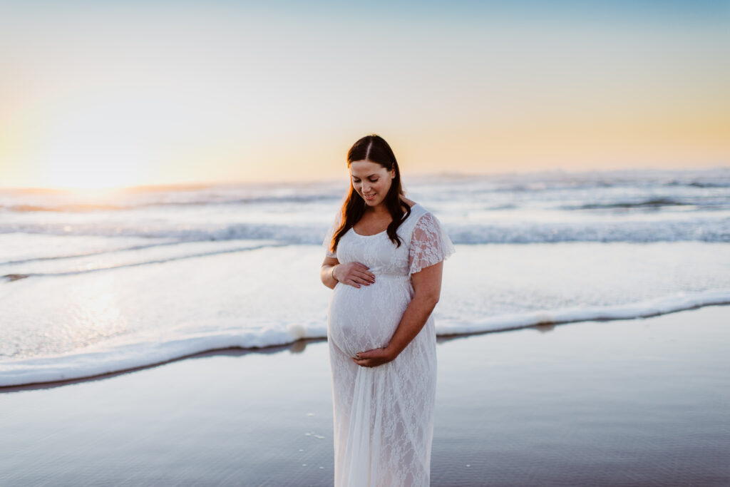 Image of pregnant woman on the beach at sunset holding her belly lovingly 